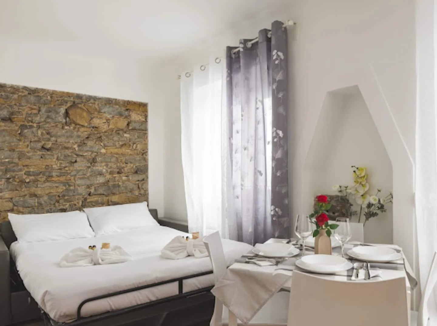 Zona giorno con divano letto, parete in pietra e tavolo vicino alla finestra